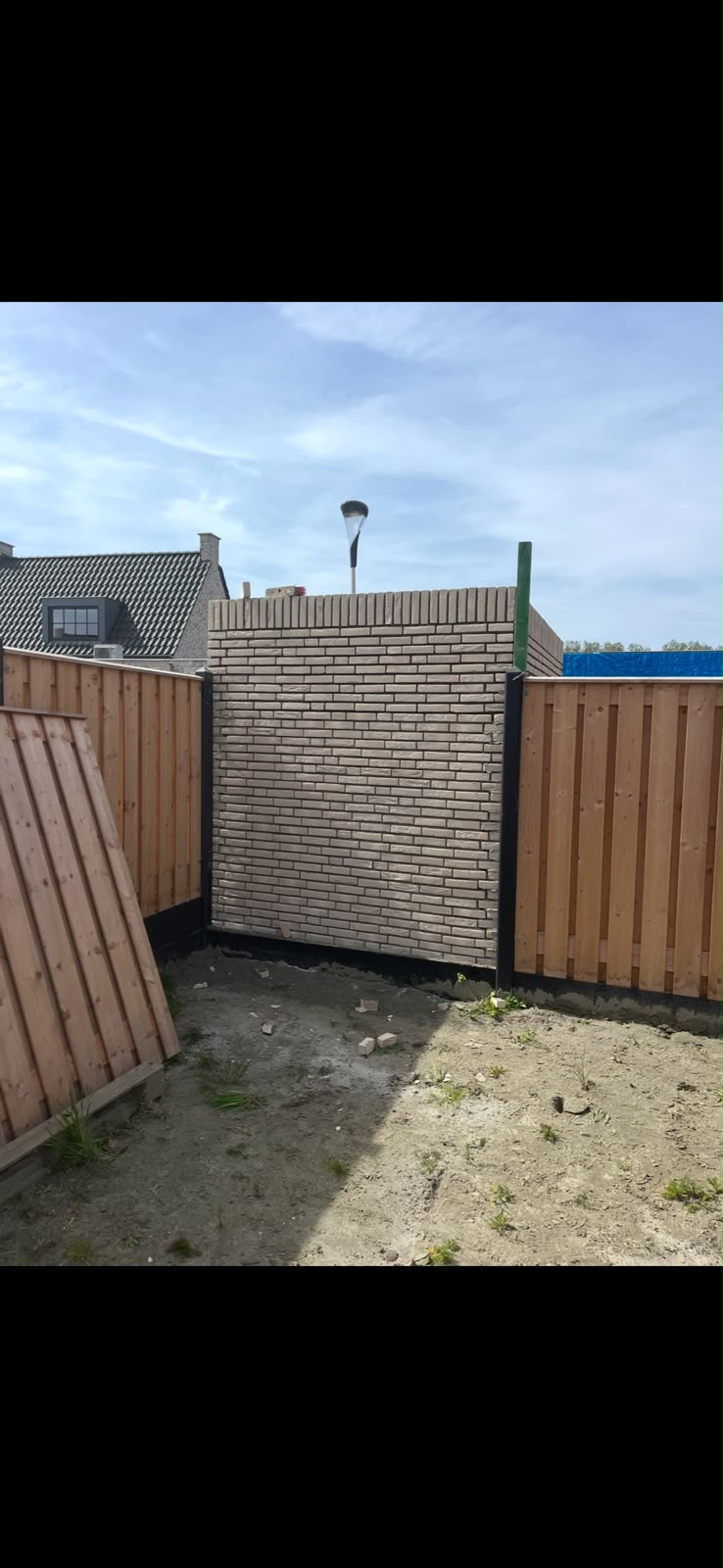 Eerste opgemetselde muurvak van de schuur tussen de tuinschuttingen, met bouwprofiel
