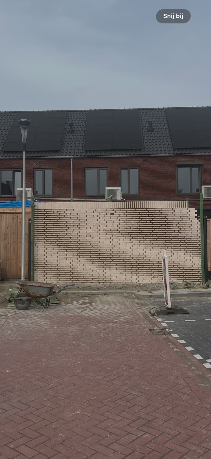 De gemetselde schuur van familie Baartmans gezien vanaf de straat, met de nieuwbouwwoning en zonnepanelen op de achtergrond